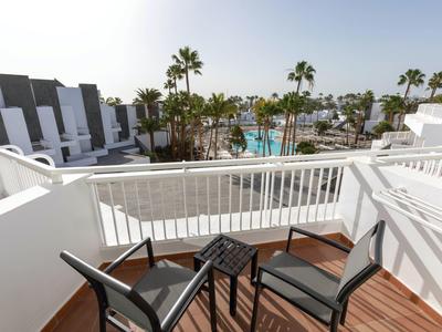 Balcone con due sedie e un piccolo tavolo con vista su piscina e palme.