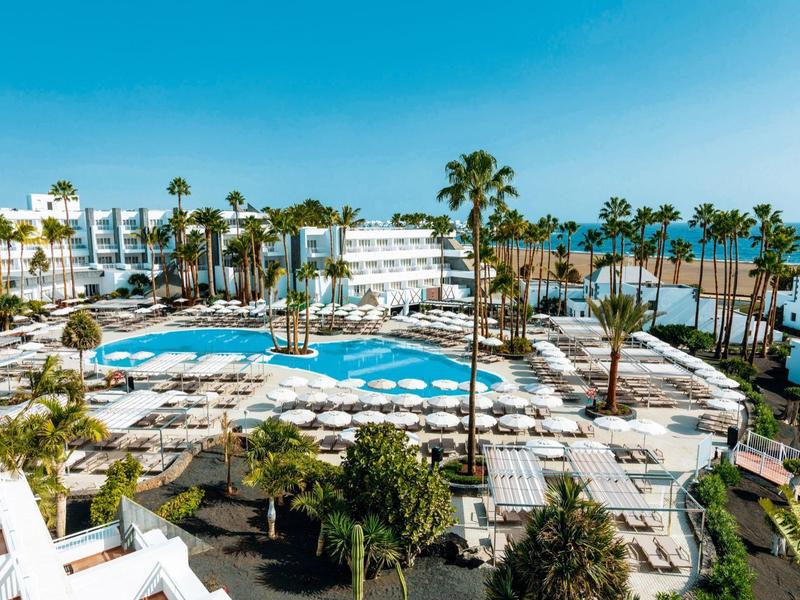 Grande piscina dell'hotel con lettini, palme, vista sul mare e cielo azzurro.