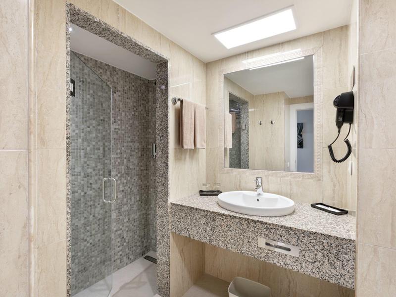 Bagno luminoso con doccia in vetro, specchio grande e lavabo con asciugacapelli.