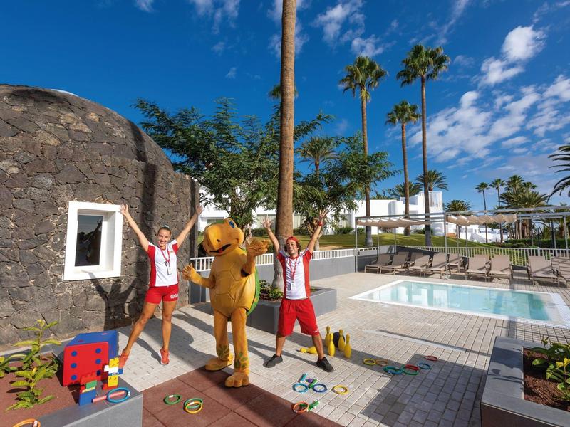 Due persone posano accanto a una mascotte vicino alla piscina con il sole.