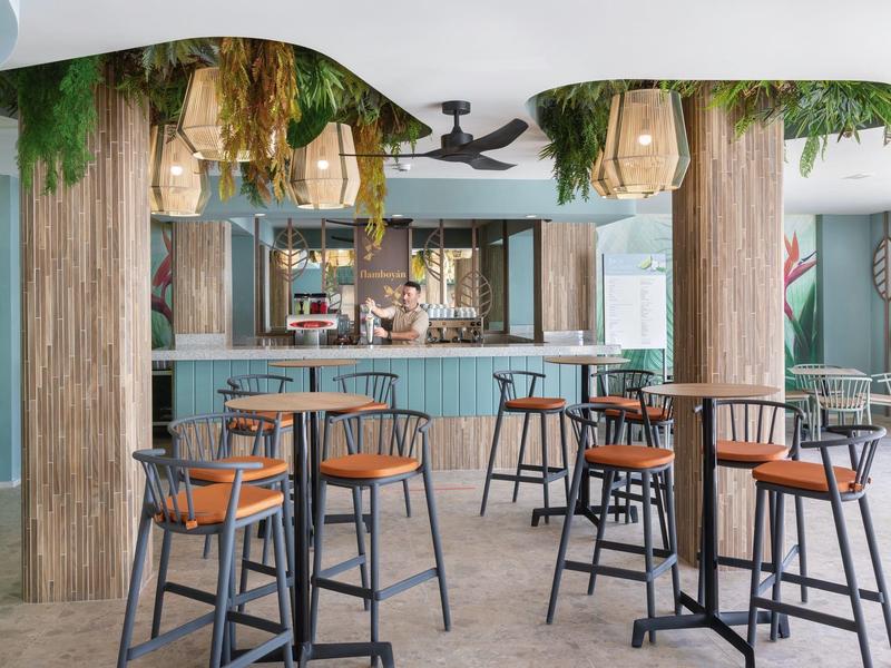 Area bar d'hotel moderna con sedute blu e decorazioni naturali di piante sospese.