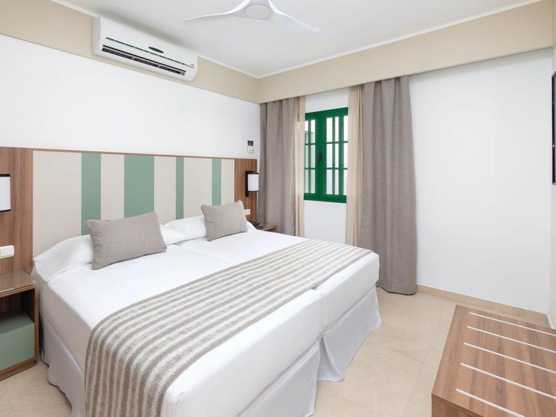 Camera d'albergo luminosa con letto matrimoniale, testiera a strisce verdi e grande finestra.