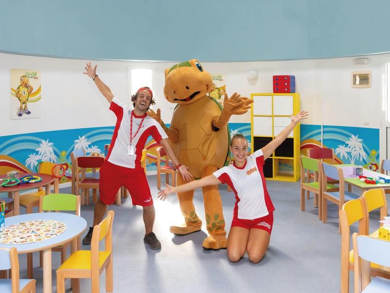 Angolo giochi colorato per bambini con due animatori e una mascotte in un hotel.