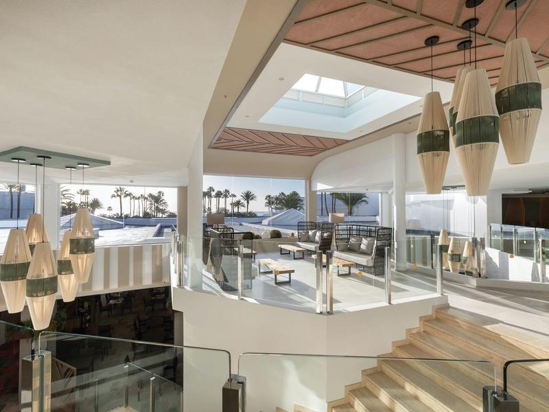 Hall dell'hotel moderna con spazi aperti, scale e vista sull'acqua alla luce del giorno.