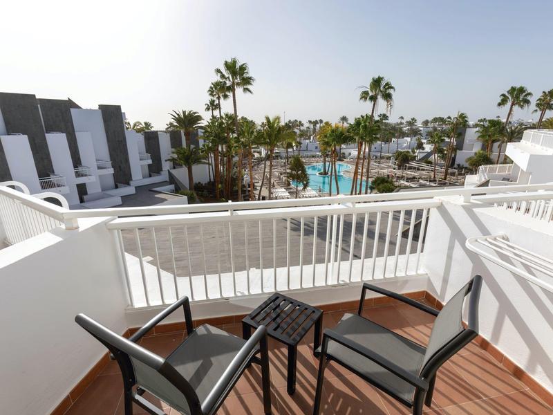 Balcone con due sedie e un piccolo tavolo con vista su piscina e palme.