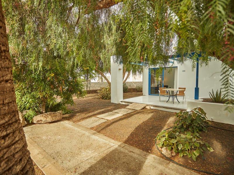 Patio esterno con tavolo e sedie davanti a un edificio bianco circondato da alberi e piante.
