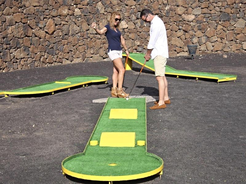 Due persone che giocano a mini golf su una superficie di pietra nera con un muro di pietra sullo sfondo.