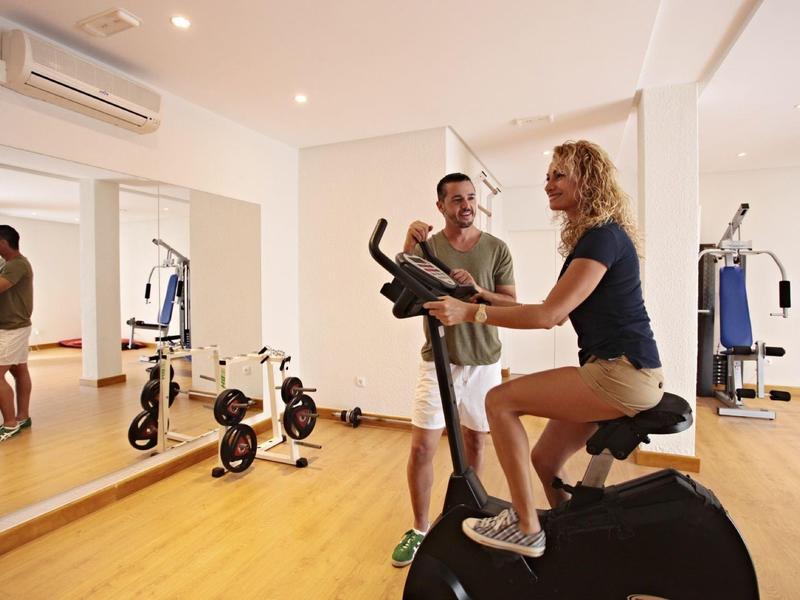 Coppia che si allena su macchine palestra in una sala fitness luminosa con pavimento in legno.