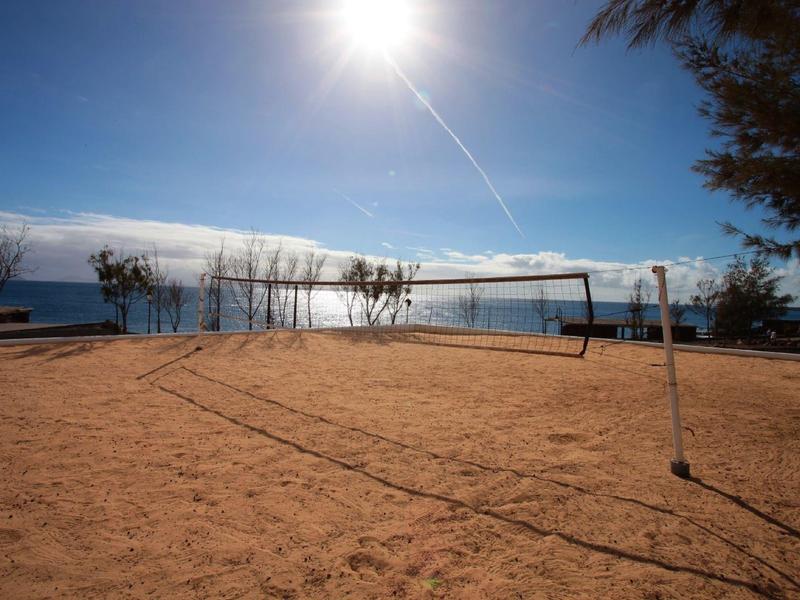 Campo da beach volley soleggiato vicino al mare con cielo azzurro e alberi.
