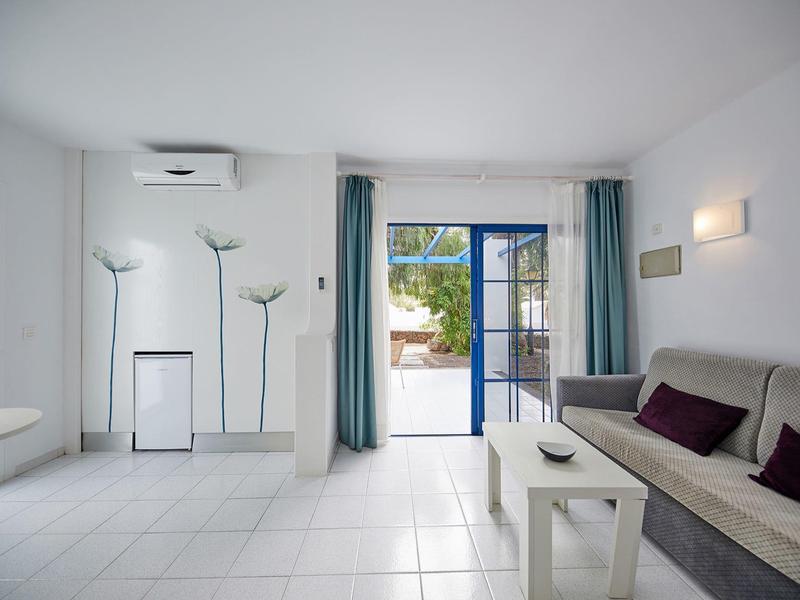 Soggiorno luminoso con divano, tavolino, lampade da terra e porta finestra verso l'esterno.