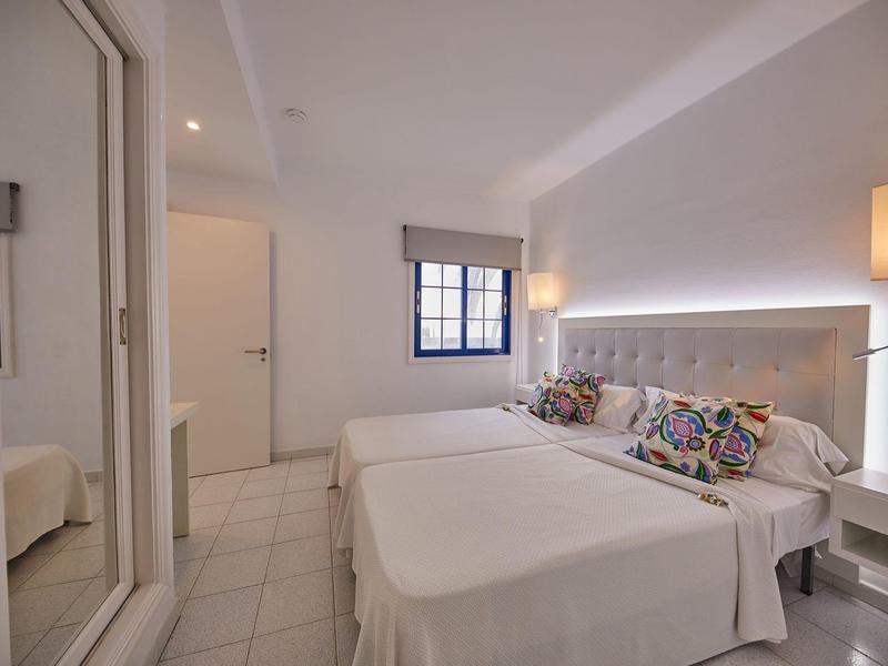 Camera d'hotel luminosa con due letti singoli, cuscini colorati e illuminazione moderna.