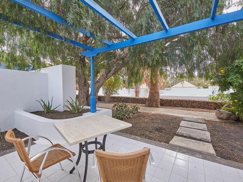 Patio esterno con tavolo, sedie, sentiero e alberi verdi rigogliosi sullo sfondo.