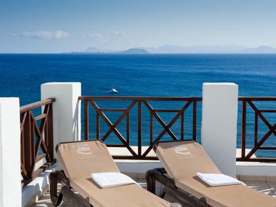 Deux chaises longues sur une terrasse avec vue sur la mer bleue et le ciel clair.