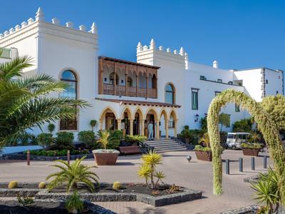 Weißes Hotelgebäude im mediterranen Stil mit Palmen und klarem blauem Himmel.