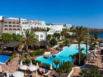 Vue panoramique d'un hôtel avec plusieurs piscines et vue sur la mer par temps ensoleillé.