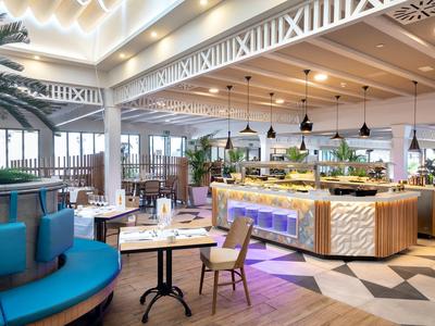 Restaurant moderne avec des couleurs vives, mobilier élégant et plafond haut avec structure en bois.