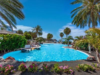 Piscine extérieure avec palmiers et soleil dans un jardin d'hôtel tropical.