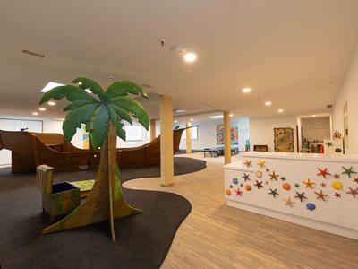 Intérieur d'un hôtel avec réception moderne et aire de jeux pour enfants décorée de palmiers.