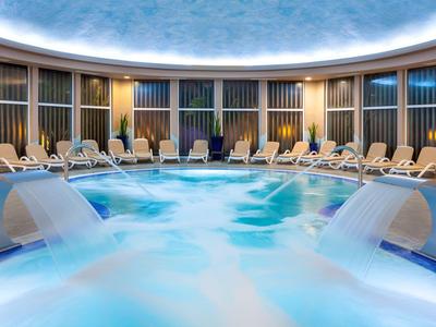 Une piscine intérieure circulaire avec des cascades et des chaises longues dans un spa d'hôtel.