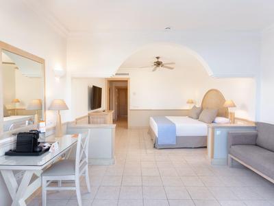 Chambre d'hôtel lumineuse et spacieuse avec lit, canapé, bureau et machine à café.