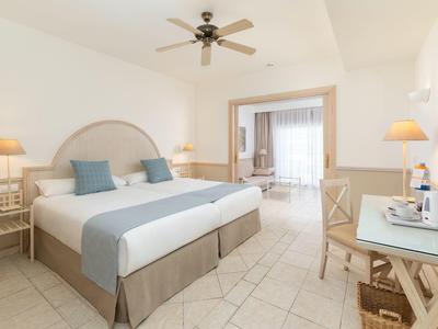 Chambre d'hôtel lumineuse avec lit double, ventilateur au plafond, bureau et ambiance calme.