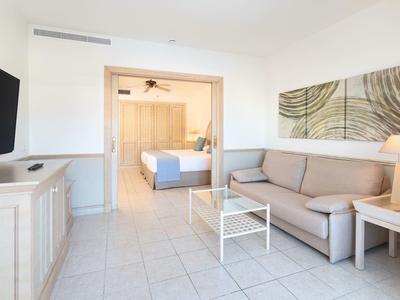 Salon lumineux avec canapé, table basse, télévision et accès ouvert à une chambre.