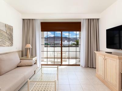 Salon lumineux avec canapé, table basse en verre, TV et vue sur balcon à travers de grandes fenêtres