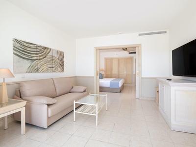 Chambre d'hôtel lumineuse avec canapé, table, télévision et vue sur une chambre séparée.