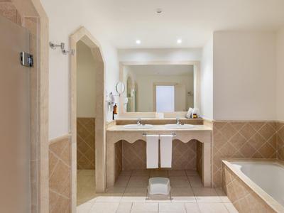 Salle de bain lumineuse avec grand miroir, lavabo, baignoire et murs carrelés beiges.
