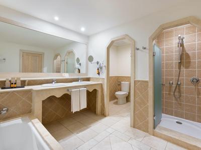Salle de bain lumineuse avec douche, baignoire et grand miroir au-dessus du lavabo.