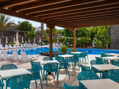 Terrasse couverte avec tables et chaises à côté d'une piscine et de transats dans un hôtel.