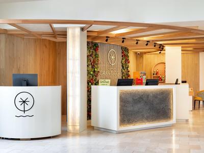Modern hotel reception area with white counters, wood paneling, and a plant wall.