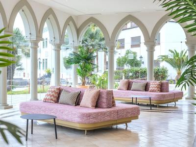 Covered terrace with pink sofas, cushions, and large plants in a bright, open space.
