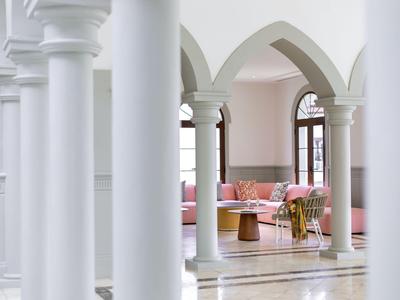 White colonnade with a view of a bright room featuring pink sofas and a table.