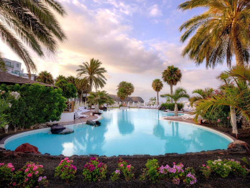 Grand piscine dans un cadre tropical avec des palmiers et des fleurs, vue sur la mer.