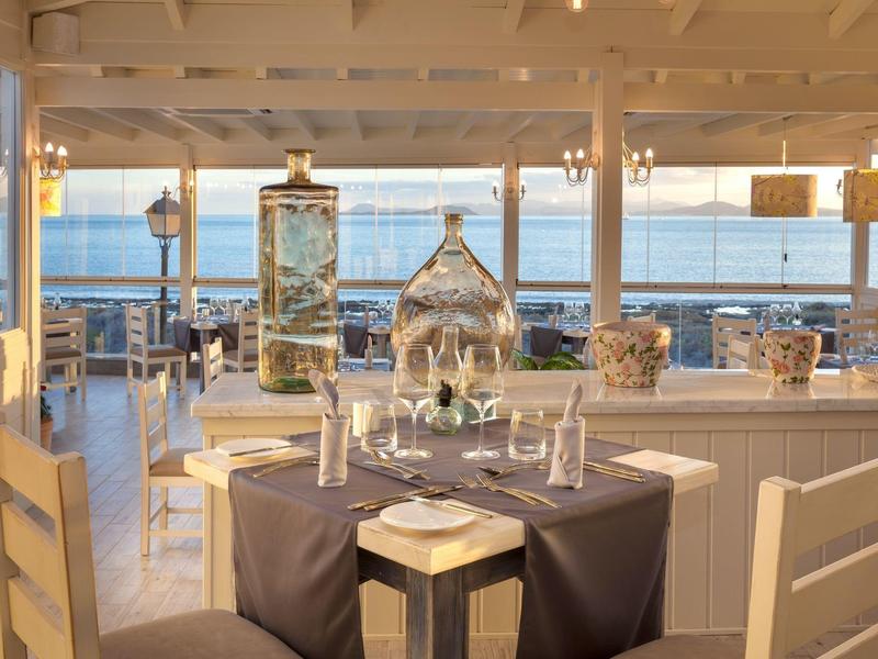 Restaurant élégant avec tables dressées et vue sur la mer au coucher du soleil.