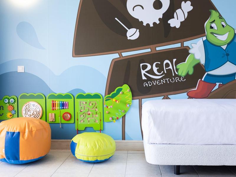 Coin jeux pour enfants avec coussins colorés et fresque de pirate à côté d’un canapé blanc.