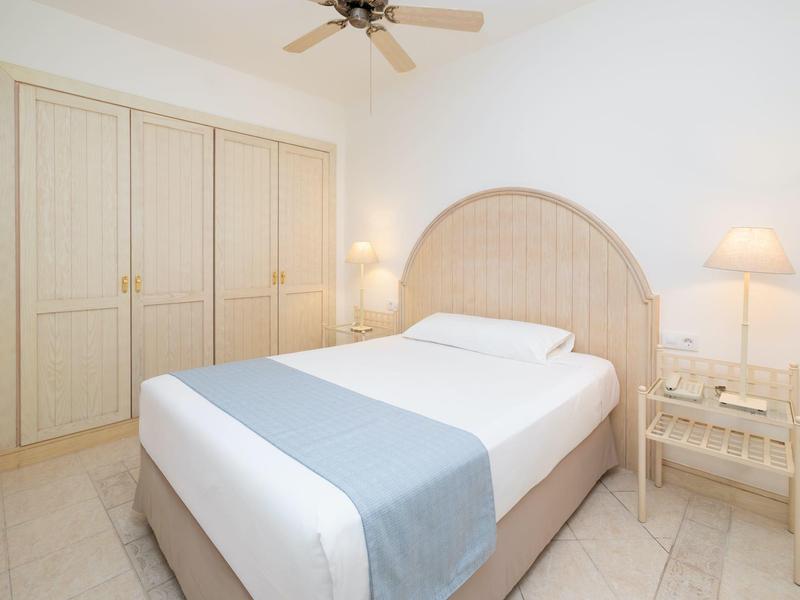 Chambre d'hôtel lumineuse avec lit double, armoire et lampes de chevet aux tons neutres.