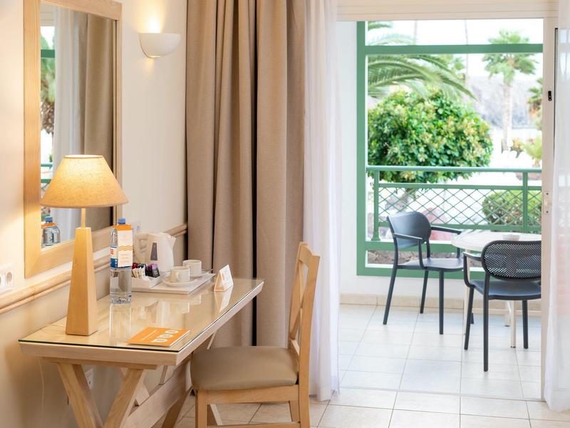 Une pièce d'hôtel lumineuse avec une table en bois, une chaise et une vue sur une terrasse avec des chaises.