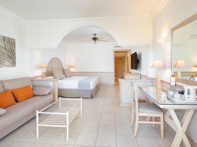 Chambre d'hôtel lumineuse avec canapé, lit, bureau et climatisation.