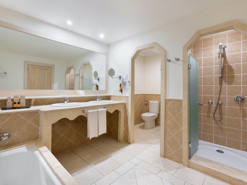 Salle de bain lumineuse avec douche, baignoire et grand miroir au-dessus du lavabo.