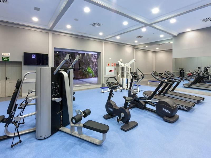 Salle de sport moderne avec divers appareils d'entraînement et un sol bleu.