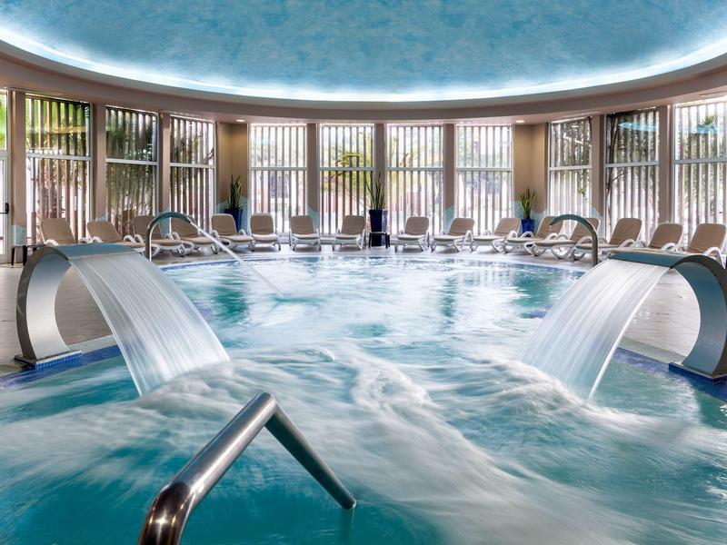 Piscine intérieure avec jeux d'eau et puits de lumière circulaire encastré dans un hôtel.