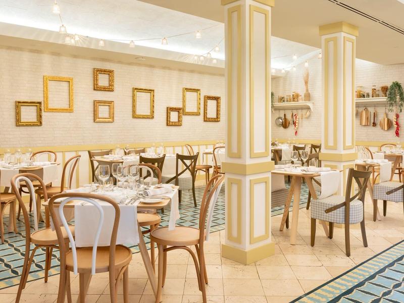 Café élégant avec des chaises en bois, des tables blanches et des murs décorés de cadres.