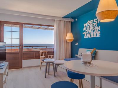 Salon moderne avec mur d’accent bleu, table à manger et vue sur la mer à travers des portes coulissantes.