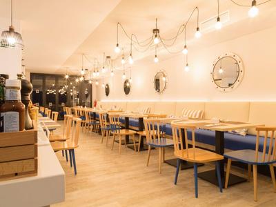 Helles Restaurant mit Holztischen und Stühlen, Sitzbänken mit blauen Polstern und Wandspiegeln.