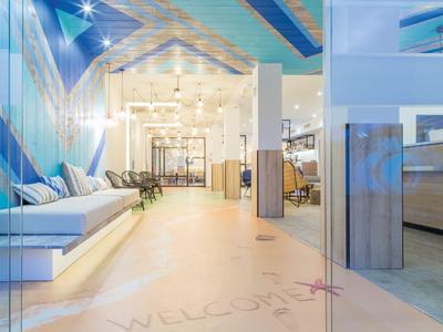 Hall d'hôtel moderne avec des couleurs claires, coin salon et texte de bienvenue au sol.