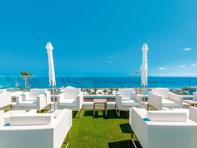 Moderne Terrasse mit weißen Möbeln, grüner Kunstrasenfläche und Blick auf das blaue Meer.