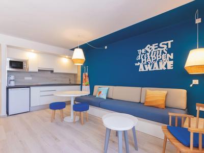 Modern eingerichtetes Wohnzimmer mit blauem Sofa, Holzmöbeln und weiß-blauem Wandzitat.
