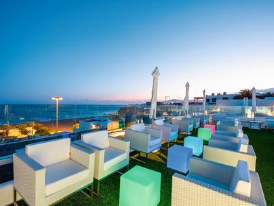 Leerer moderner Außenbereich mit weißen Sofas und bunten Hockern bei Sonnenuntergang am Meer.